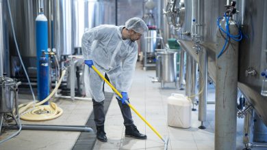 Professional industrial cleaner in protective uniform cleaning floor of food processing plant.